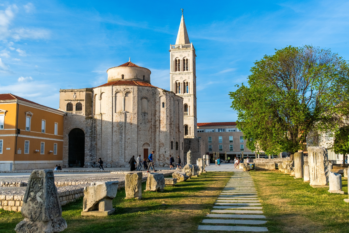 Church of St. Donatus in Zadar, Croatia, with Romanesque architecture, a bell tower, ancient ruins, and a paved pathway under a clear sky.