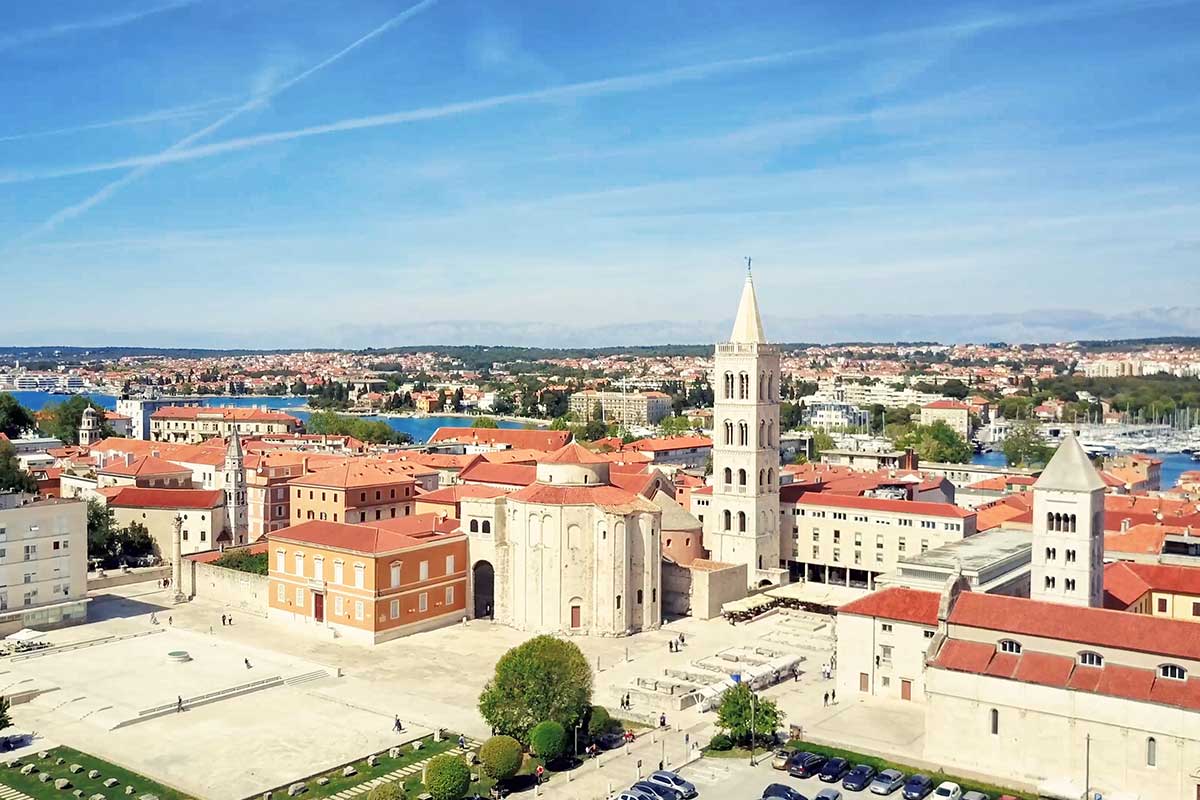 Stunning aerial view of a coastal town in Croatia with turquoise waters, a marina filled with boats, sandy beaches, and vibrant greenery.