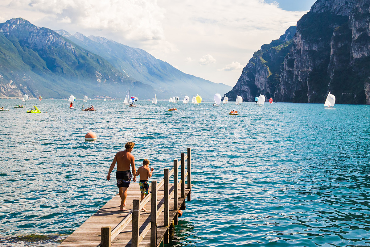 Padre e figlio stanno per fare il bagno nel Lago di Garda con vista sulle montagne