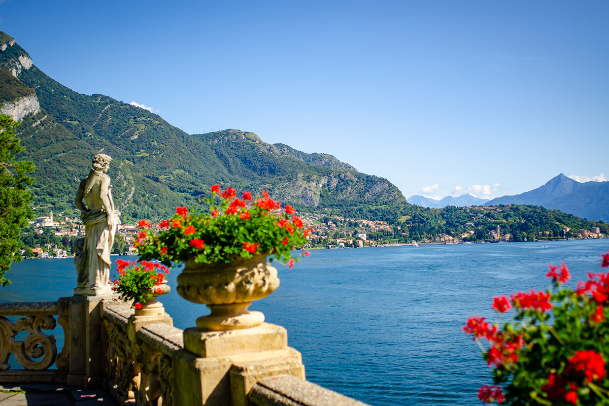 Bellissima vista lago da Villa Balbaniello sul Lago di Como con fiori rossi e statua di donna