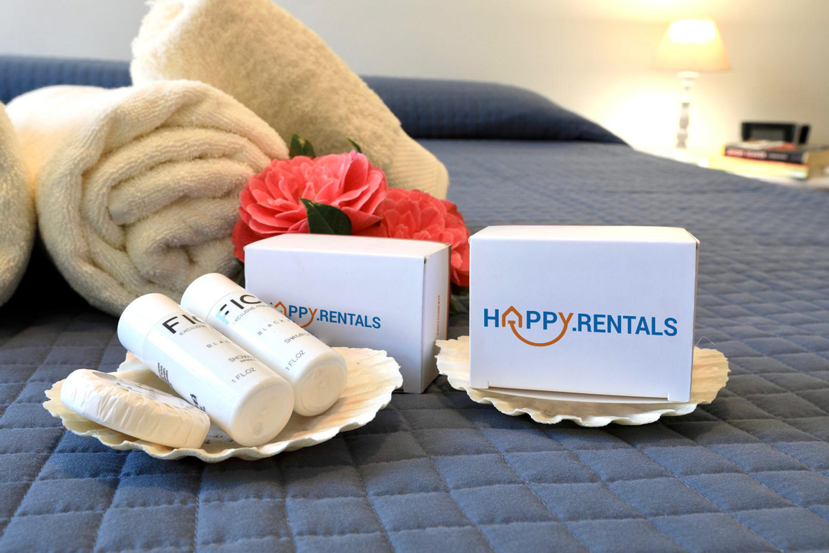 A cosy bed with Happy.Rentals' welcome bathroom kit and a set of soft towels