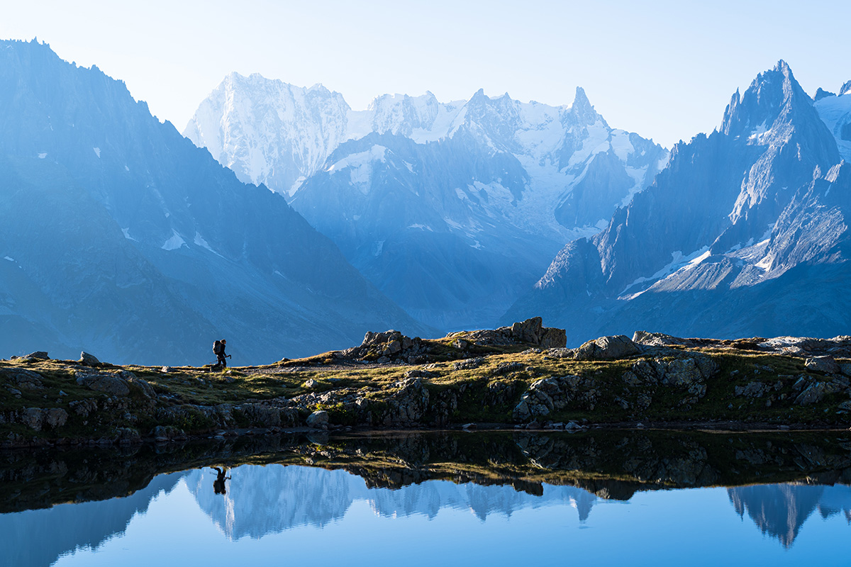 Un escursionista cammina ai bordi del bellissimo Lac des Cheserys, con il lago che riflette le montagne innevate