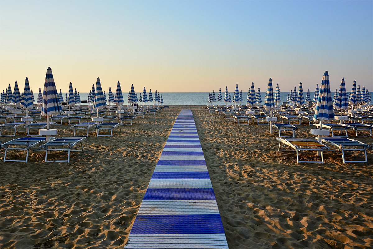 Viareggio's fine-sand beach with a boardwalk, flanked by typical blue-white sunloungers, leading to the Tyrrhenian Sea