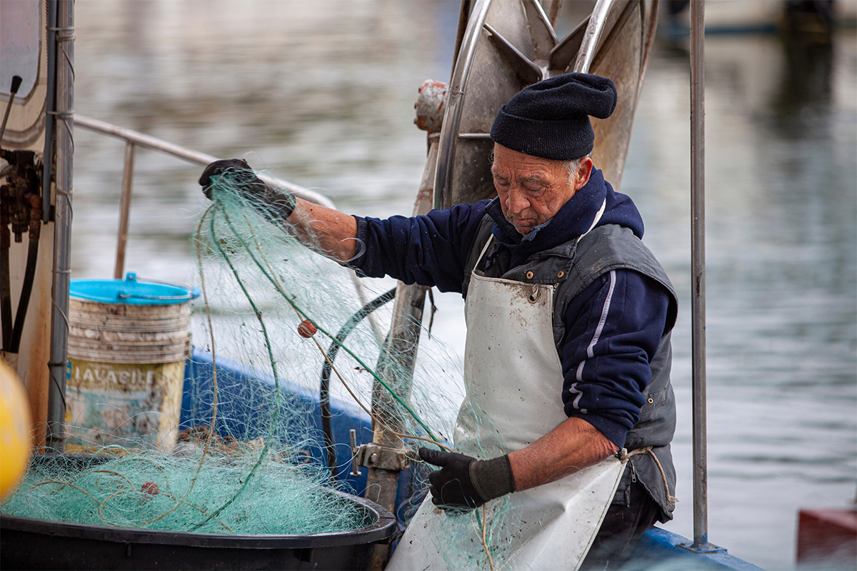 Un pescatore che districa e pulisce le reti da pesca al porto