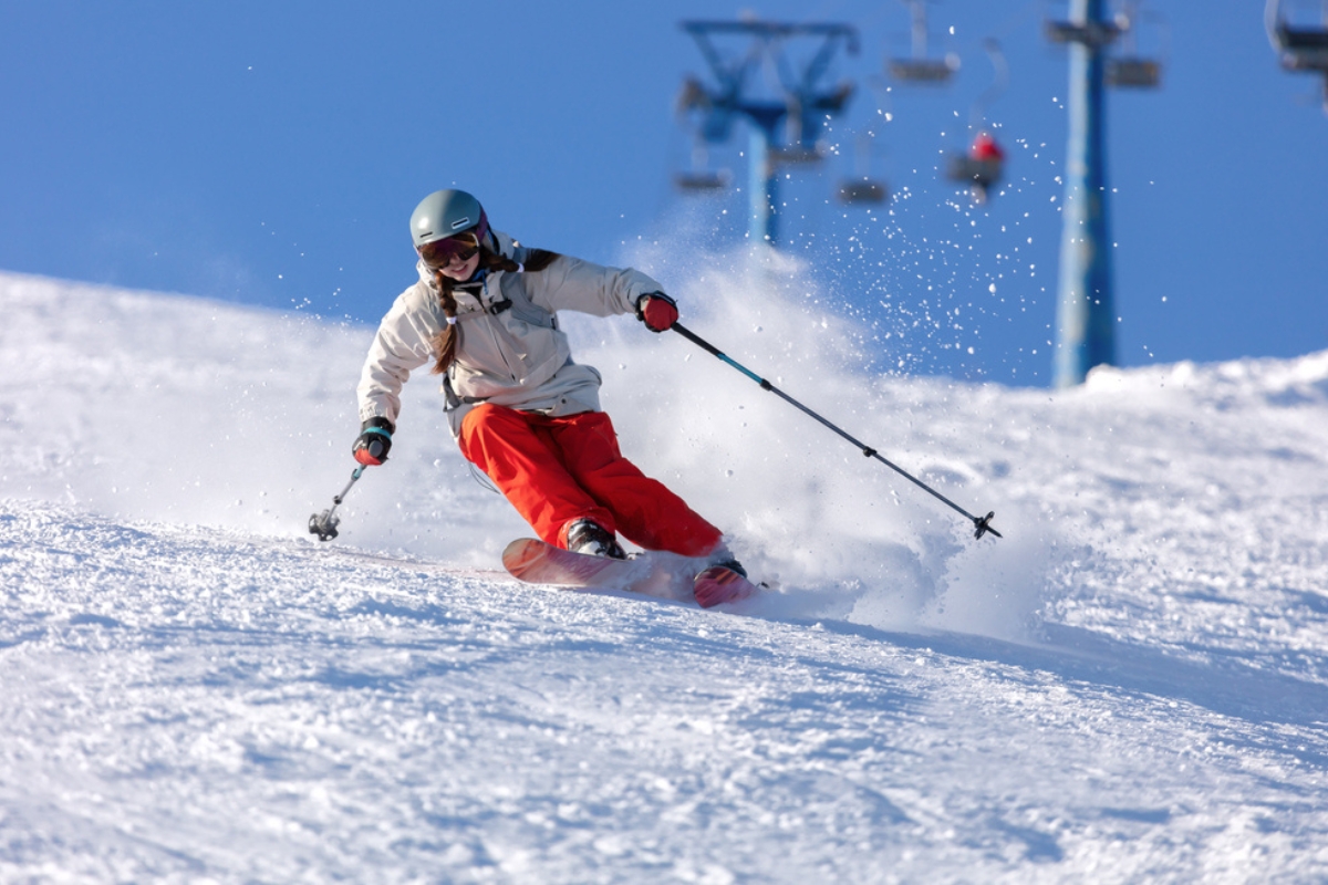 A skier in a bright suit and long pigtails on her head rides on the track with swirls of fresh snow