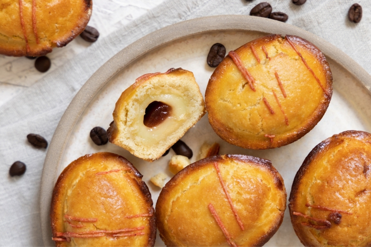 Pasticciotto leccese ripieno di crema pasticcera all'uovo e marmellata di amarene. Pasticciotti interi e a metà su un piatto. Tavolo decorato con chicchi di caffè