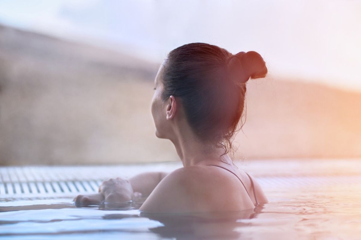 Donna che si gode la vista, rilassandosi nella piscina termale all'aperto in una giornata invernale. Montagne innevate sullo sfondo