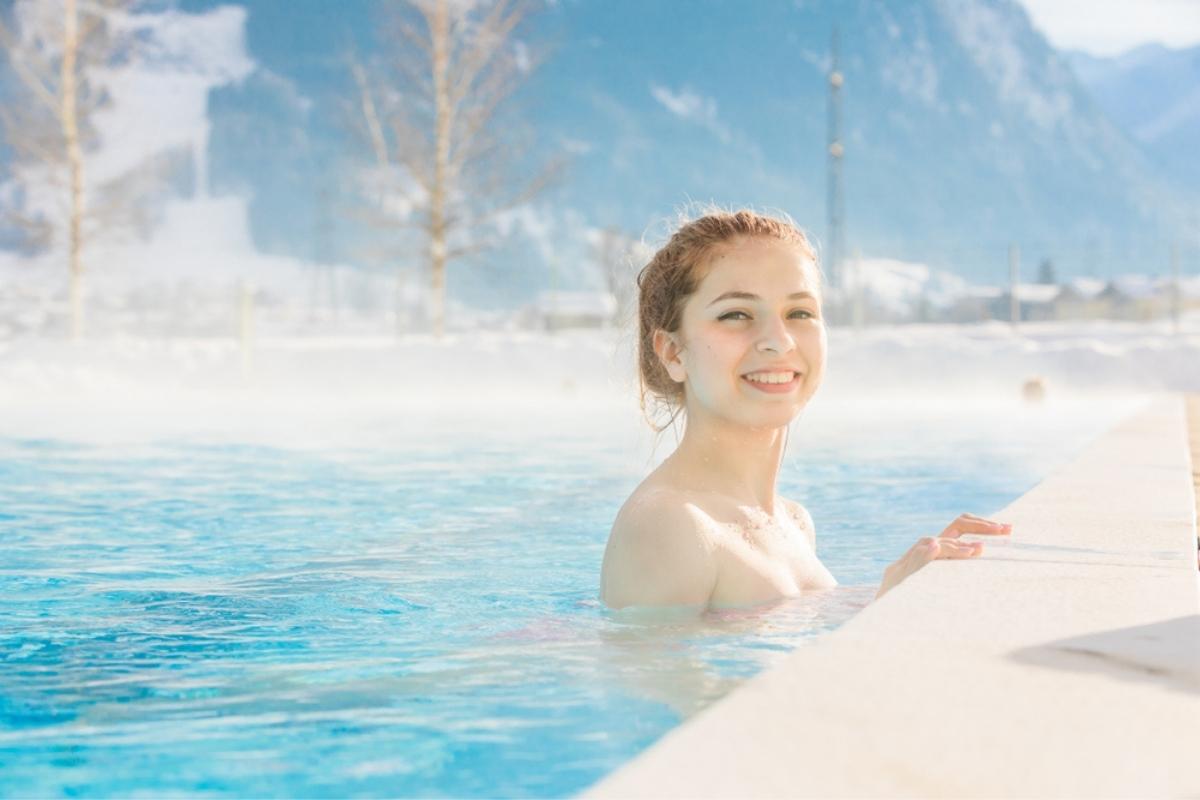 Donna sorridente che si rilassa in una piscina termale con sullo sfondo delle montagne