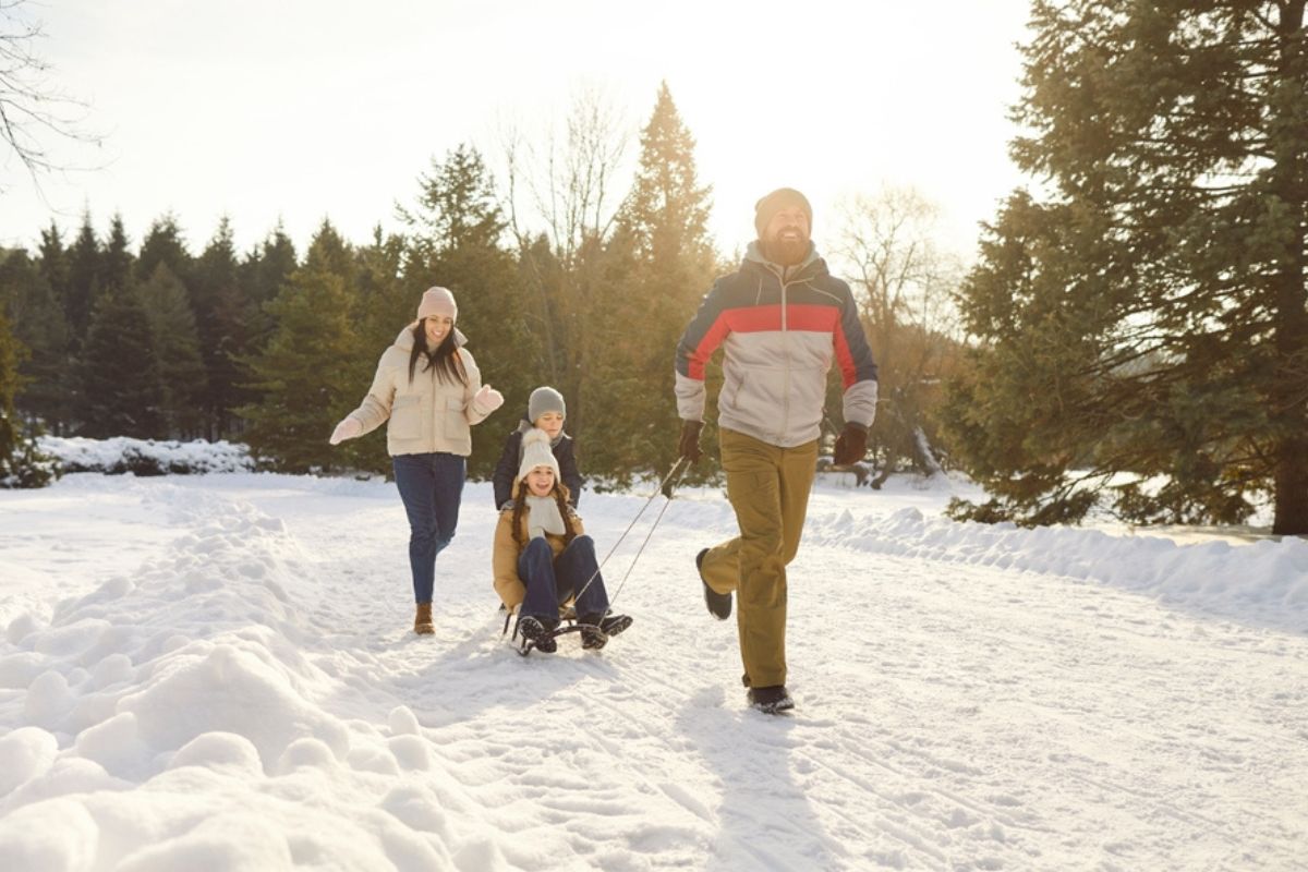 Genitori portano i bambini sulle slitte mentre passeggiano felici lungo un sentiero innevato nel parco invernale