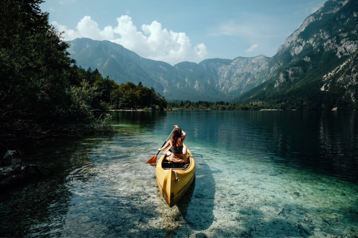 Giovane donna in canoa nel lago di Bohinj in una giornata estiva, sullo sfondo delle montagne alpine
