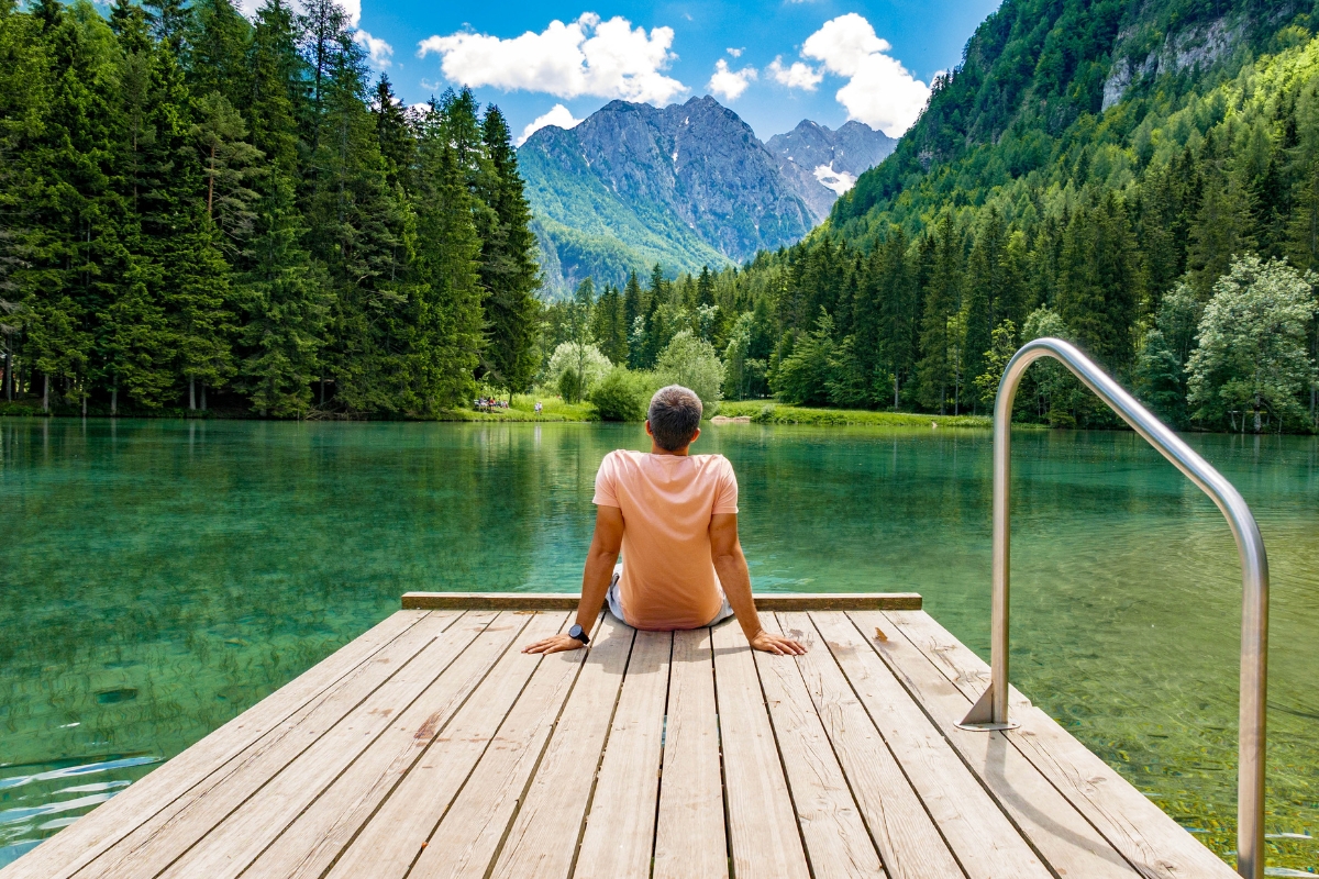 Rear view of young man sitting on wooden deck by lake Planšarsko, Jezersko, Slovenia