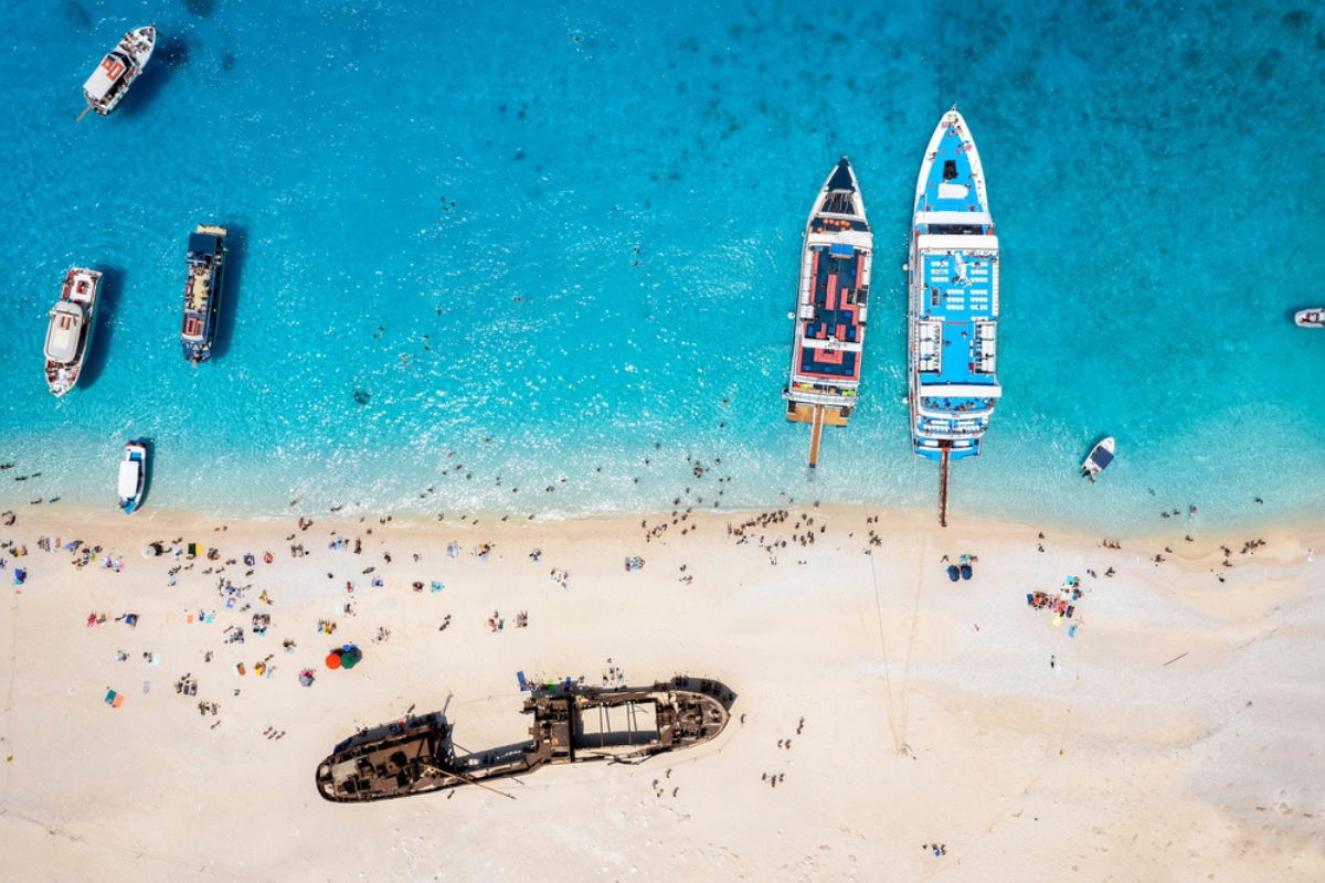 Vista aerea dall'alto della famosa spiaggia del Navagio con persone e barche da escursione che si godono il mare turchese, Zante, isole Ionie, Grecia