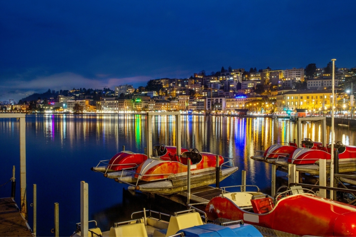 Pleasure boats (water bikes for rent) in the foreground and a stunning view of the night city of Lugano in the background