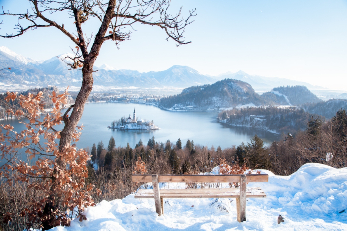 Beautiful view of wooden bench overlooking famous Lake Bled with Bled Island and Julian Alps in the background at sunrise in winter, Slovenia