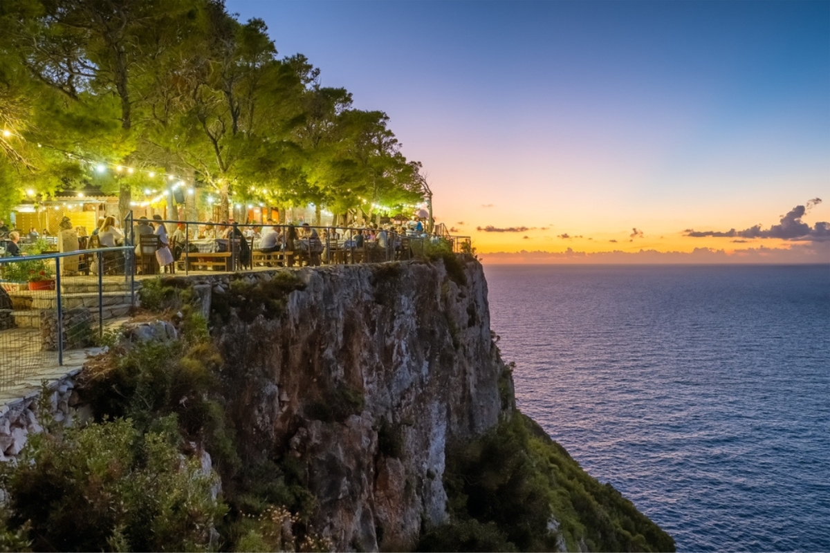 Sunset Michali Taverna on a high cliff with breathtaking sunset view of Zakynthos island coast and Ionian sea, Greece