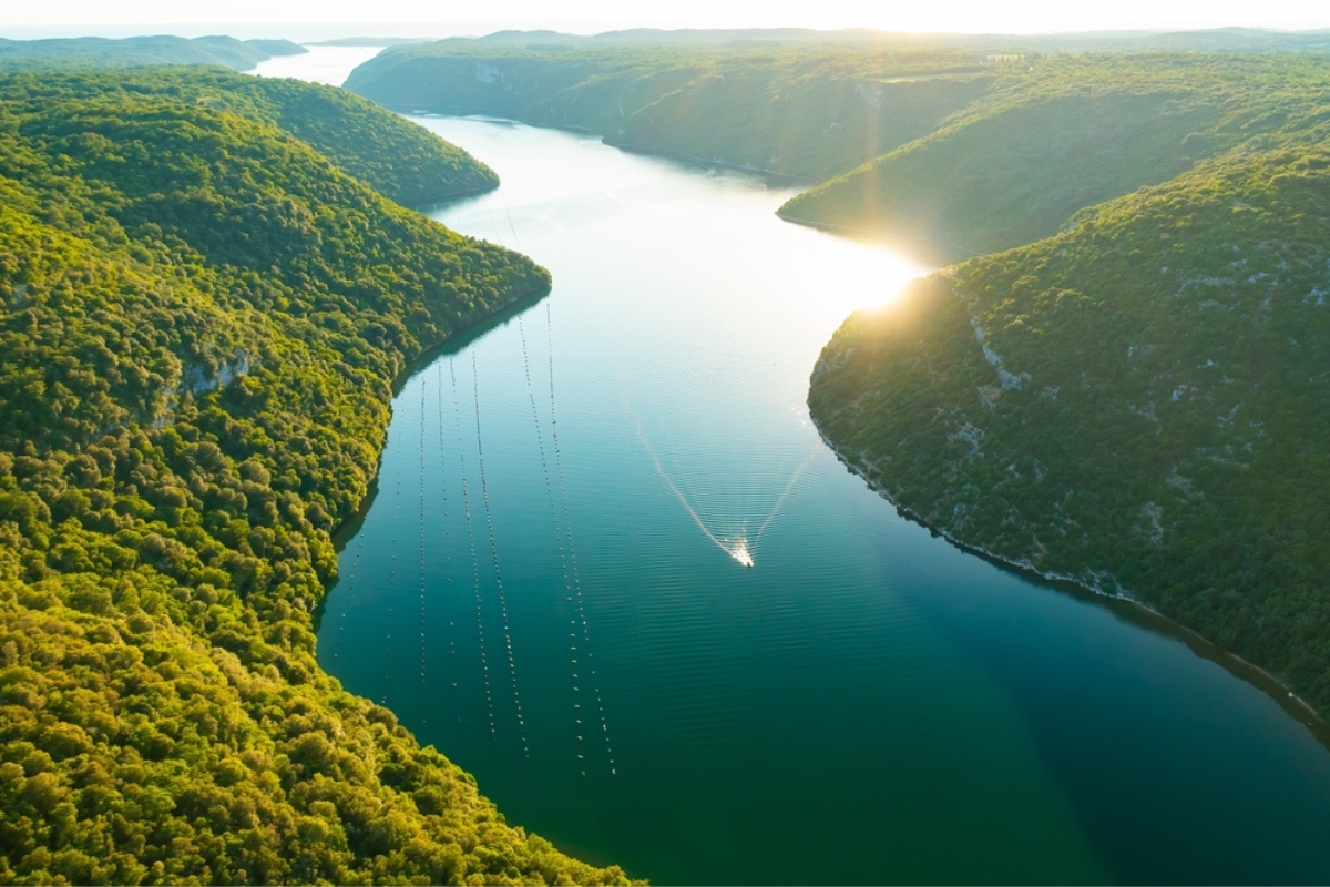 Sunset reflecting on water of Lim bay with high mountains surrounding oyster farm. Dense forests cover mountains of Istria peninsula. Aerial panorama.