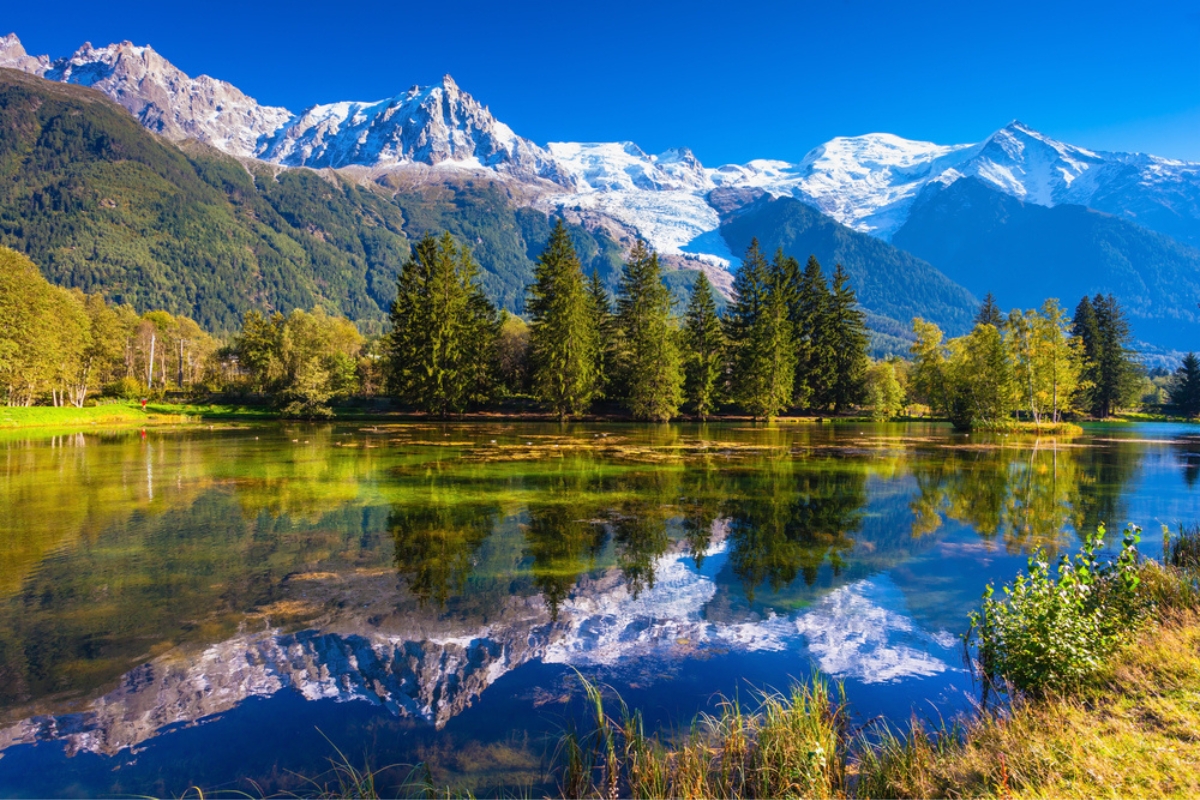 The Alps with evergreen spruce forests crowned by snowcapped mountains reflecting in a placid alpine lake