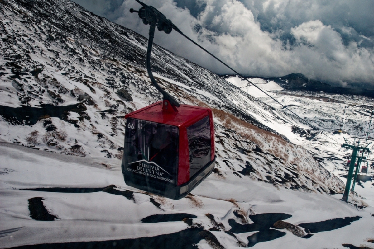 A cable car carrying tourists to Mount Etna. Surrounded by snow-capped mountains and cloudy sky