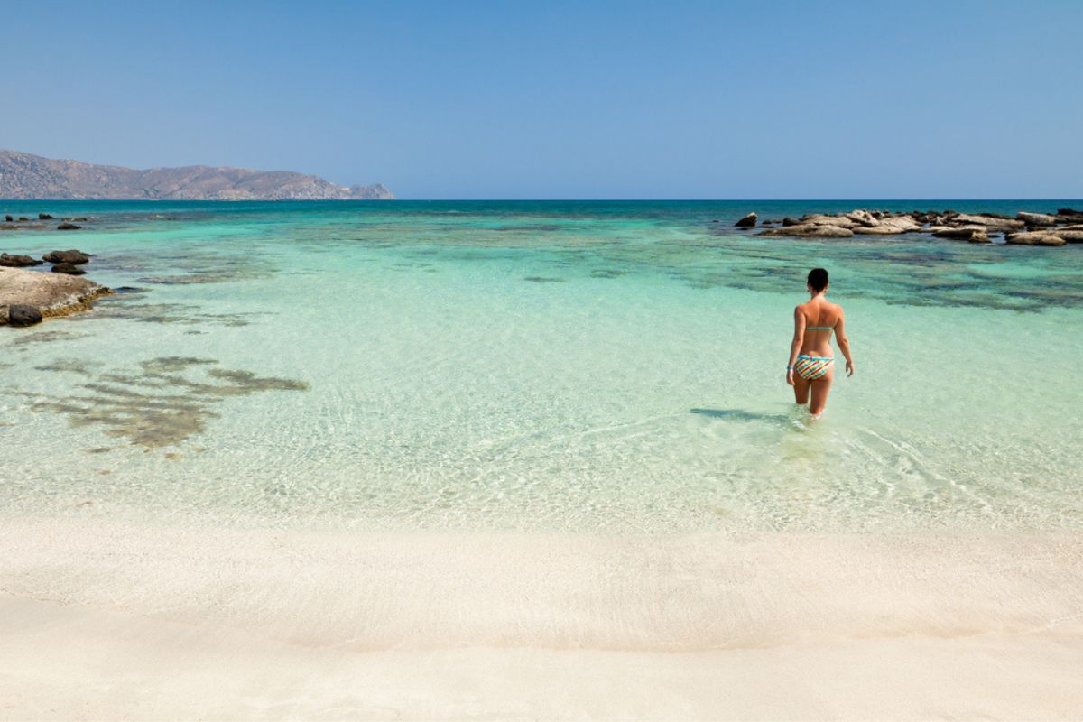Woman enjoying the the pink sand and the clear turquoise water of Elafonissi beach, Crete 