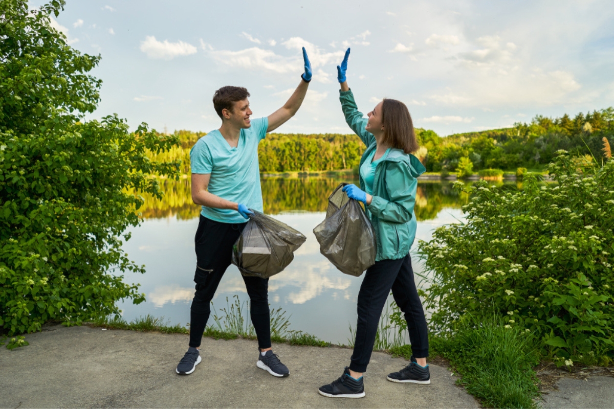 Two friends holding trash bags with lake in the background