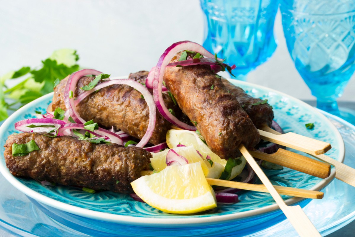 Un piatto di Ćevapčići condito con cipolla, prezzemolo e limone