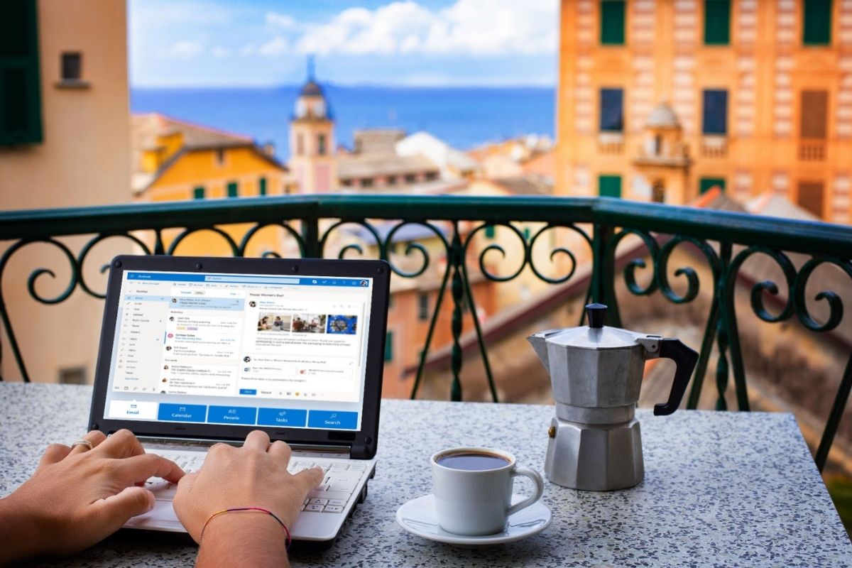 Hands typing on keyboard of a laptop on a balcony in Italy. Beautiful view and Italian coffee maker om the table.